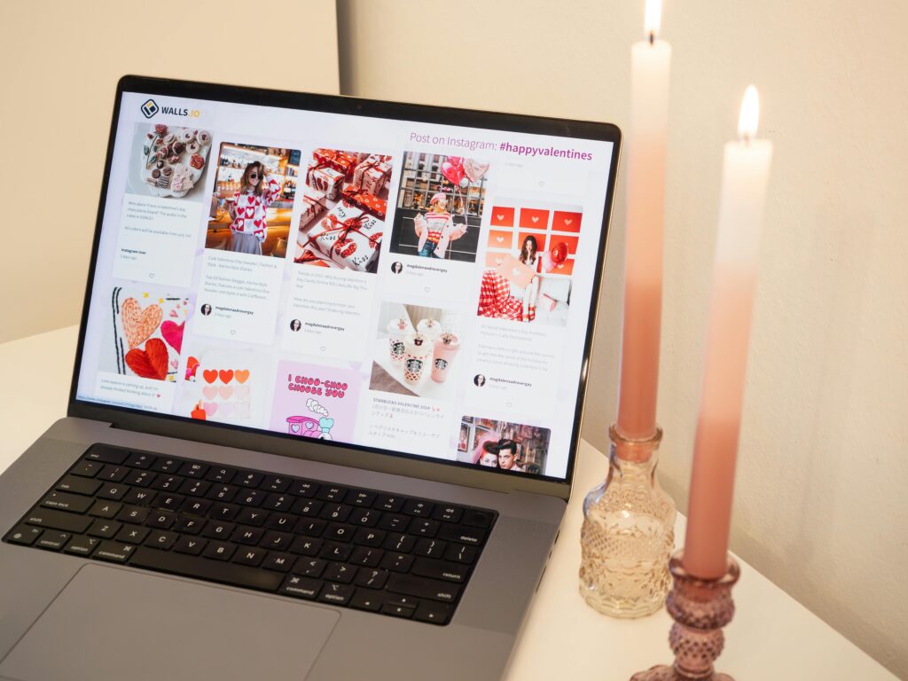 A romantic setup featuring a laptop with Valentine's posts and pink candles, perfect for a cozy atmosphere.